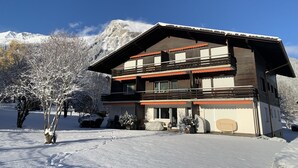 A two-story wooden chalet with a balcony, set against a snowy mountain backdrop. - Ferienwohnung Waldrand EG by Interhome (Lenk)
