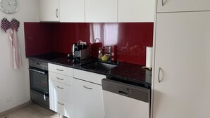 A modern kitchen with white cabinets, a red backsplash, stainless steel appliances, and a clock on the wall. - Ferienwohnung Waldrand EG by Interhome (Lenk)