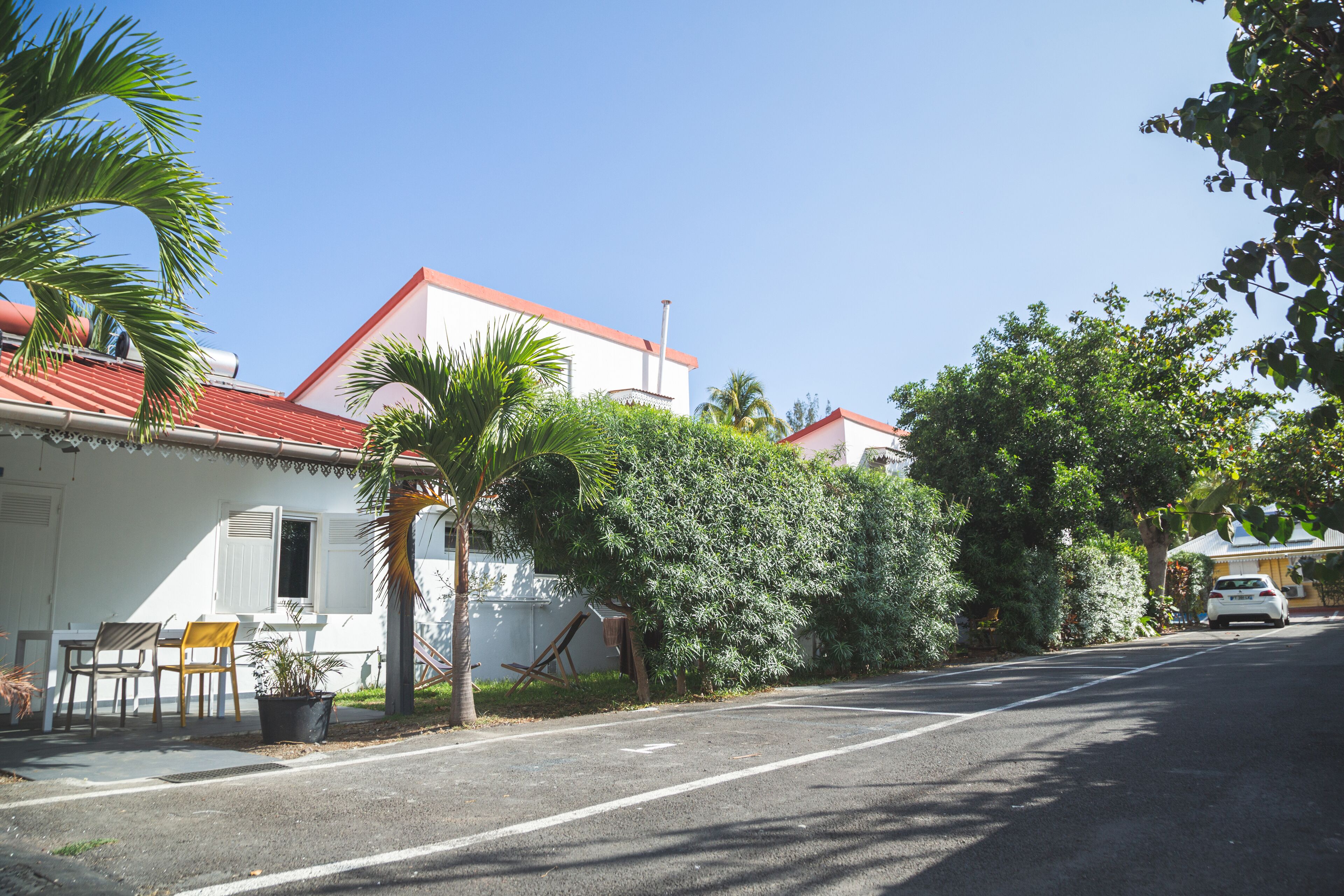 Une rue résidentielle paisible, bordée de maisons, avec une voiture garée et une végétation luxuriante.