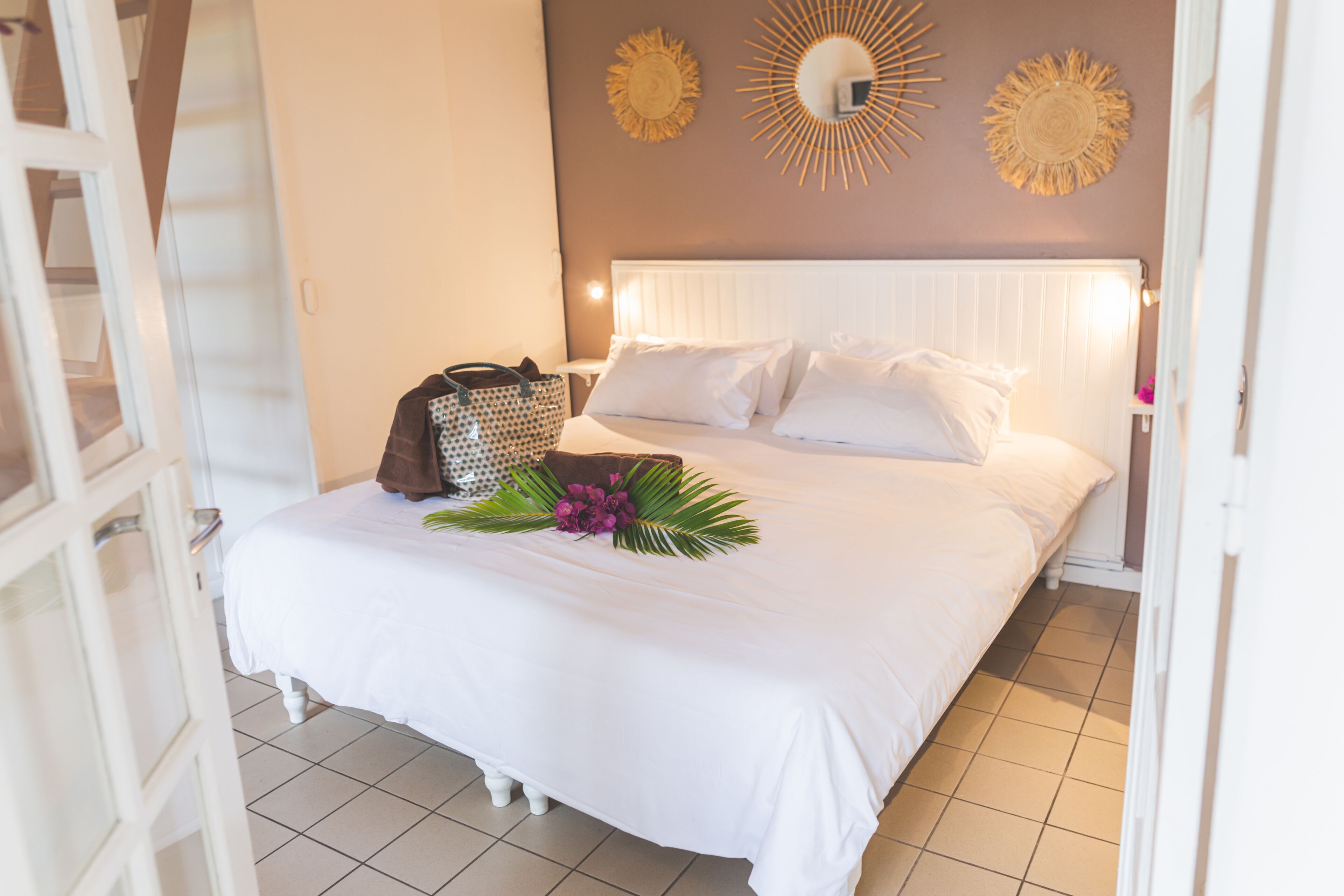 A neatly made bed with white linens, a brown bag, and a floral arrangement on the bed.
