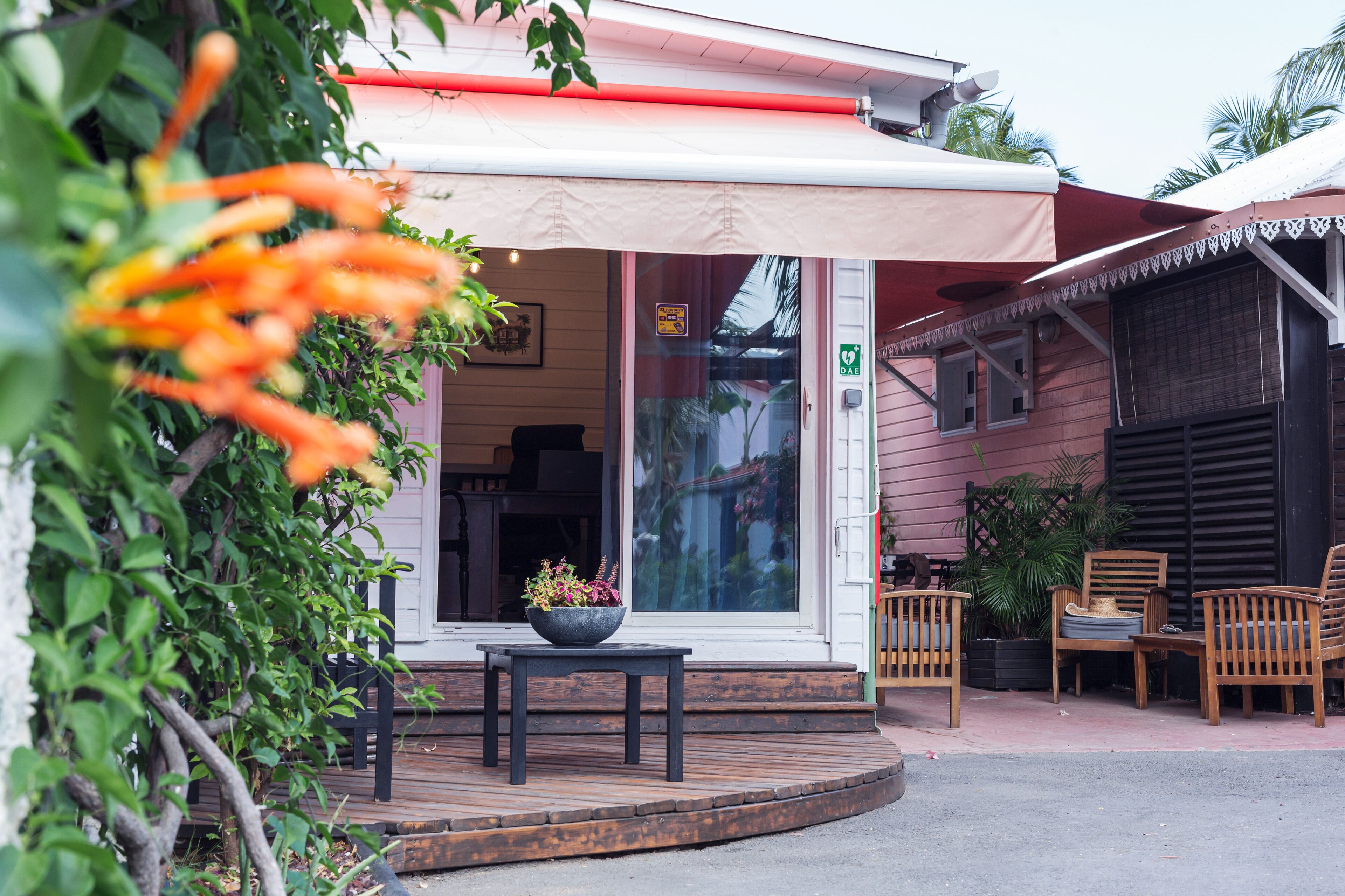 Une véranda en bois avec une table et des chaises, une plante en pot et l’entrée d’un bâtiment avec une enseigne.