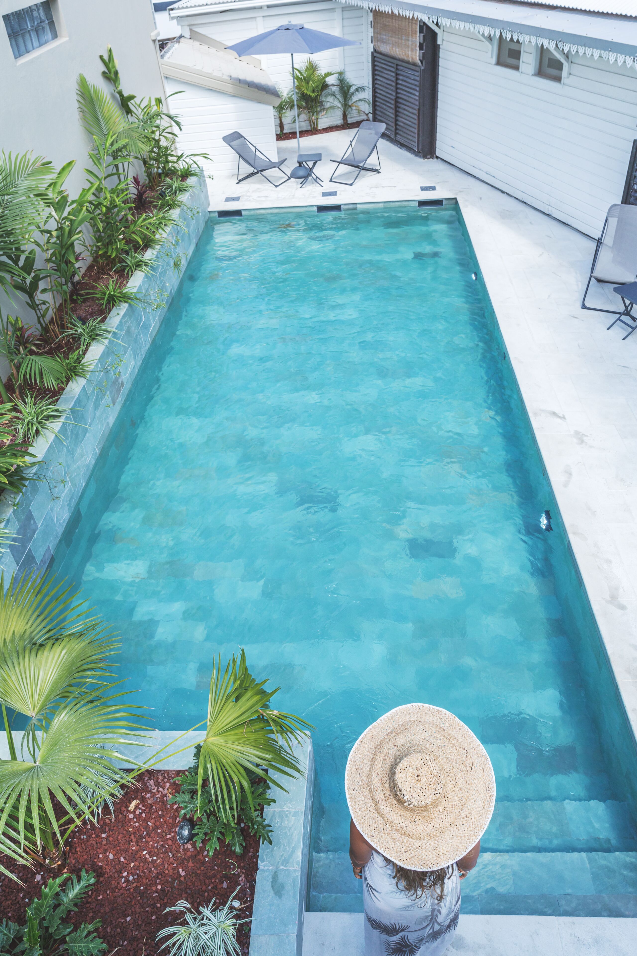 A rectangular pool with clear blue water, surrounded by a white deck and potted plants.