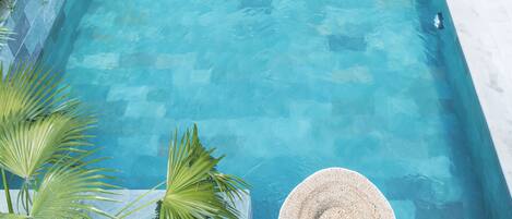 A rectangular pool with clear blue water, surrounded by a white deck and potted plants.