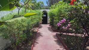 A pathway flanked by lush greenery and flowering plants, leading to a dark doorway. - Ilet du Lagon (Saint-Paul)