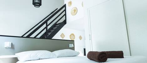 A modern hotel room with a bed, a black railing staircase, and a white wardrobe.