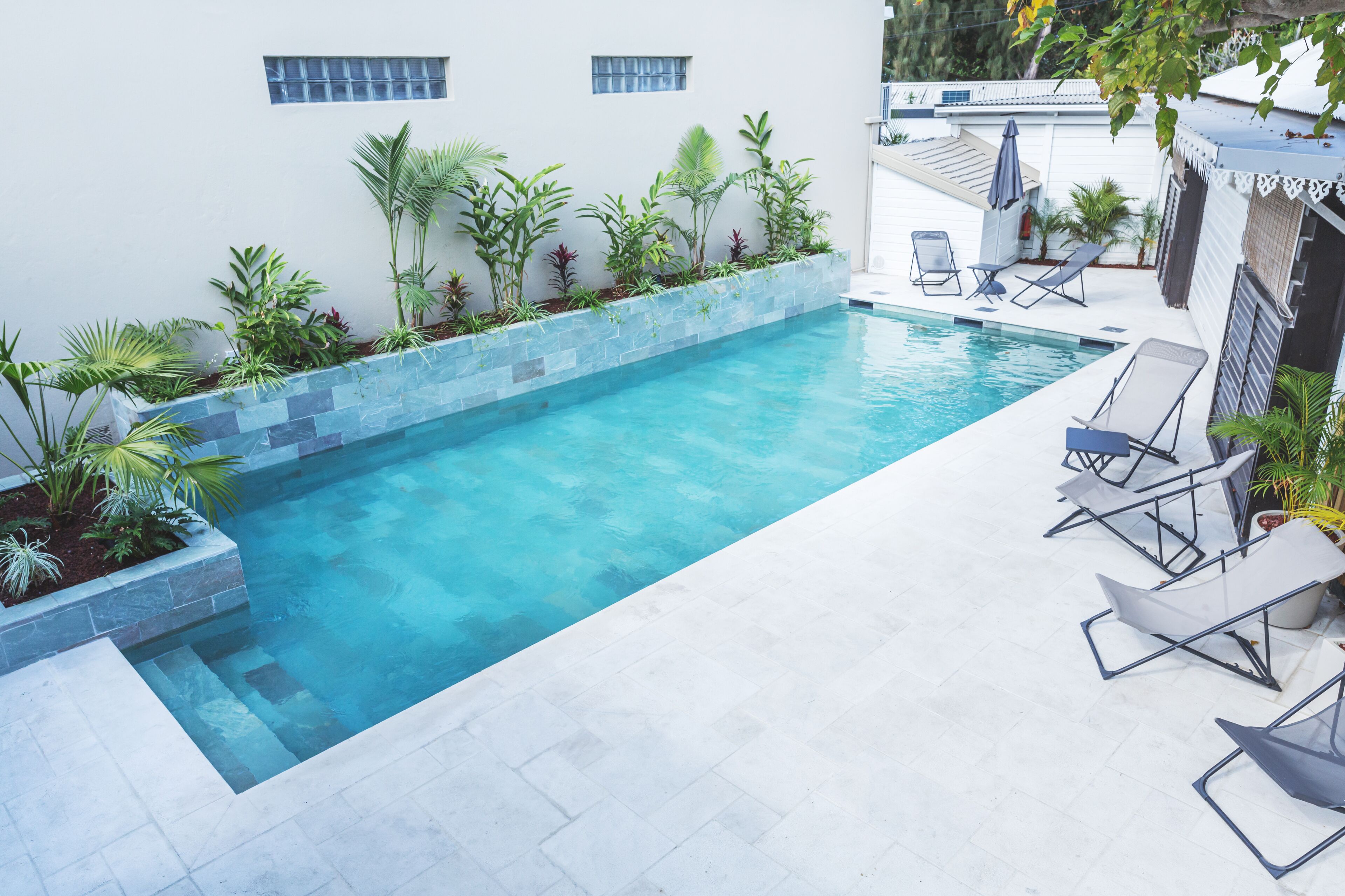 Une piscine bordée de pierres, entourée de chaises longues et de plantes en pot.