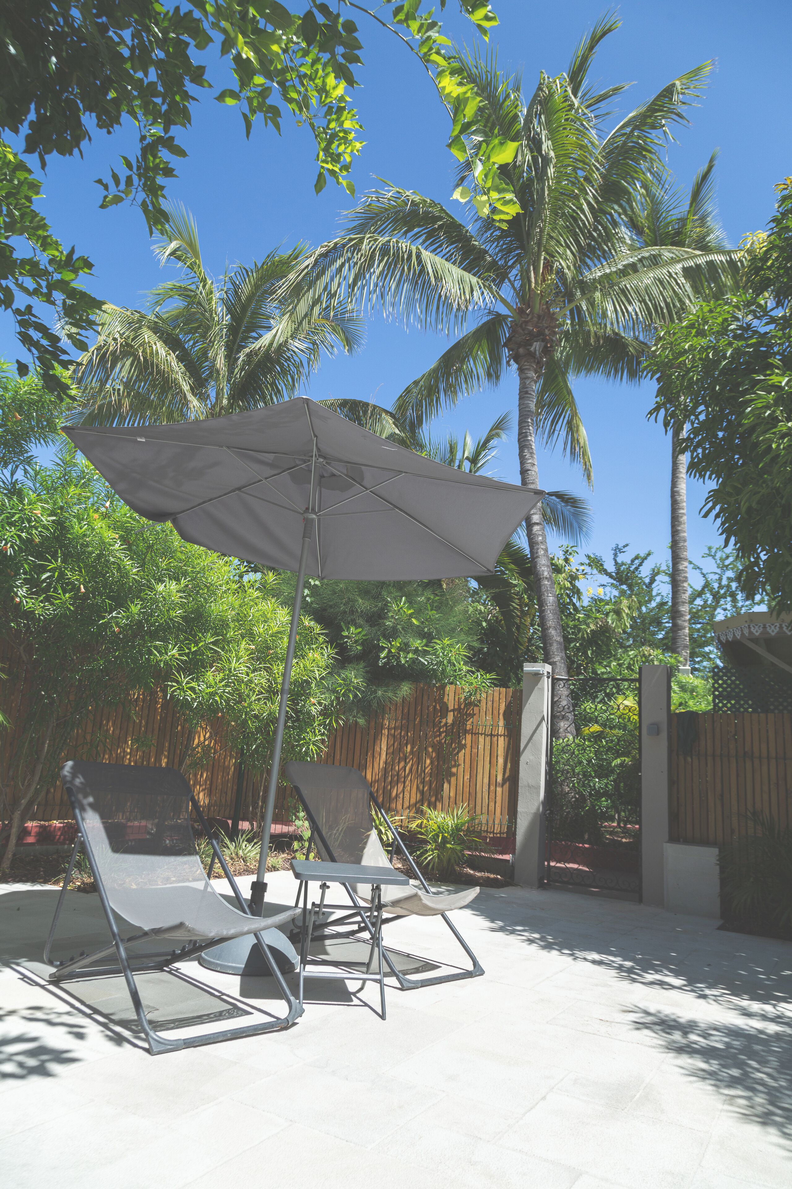 An outdoor seating area with a table and chairs, a large umbrella, and a palm tree in the background.