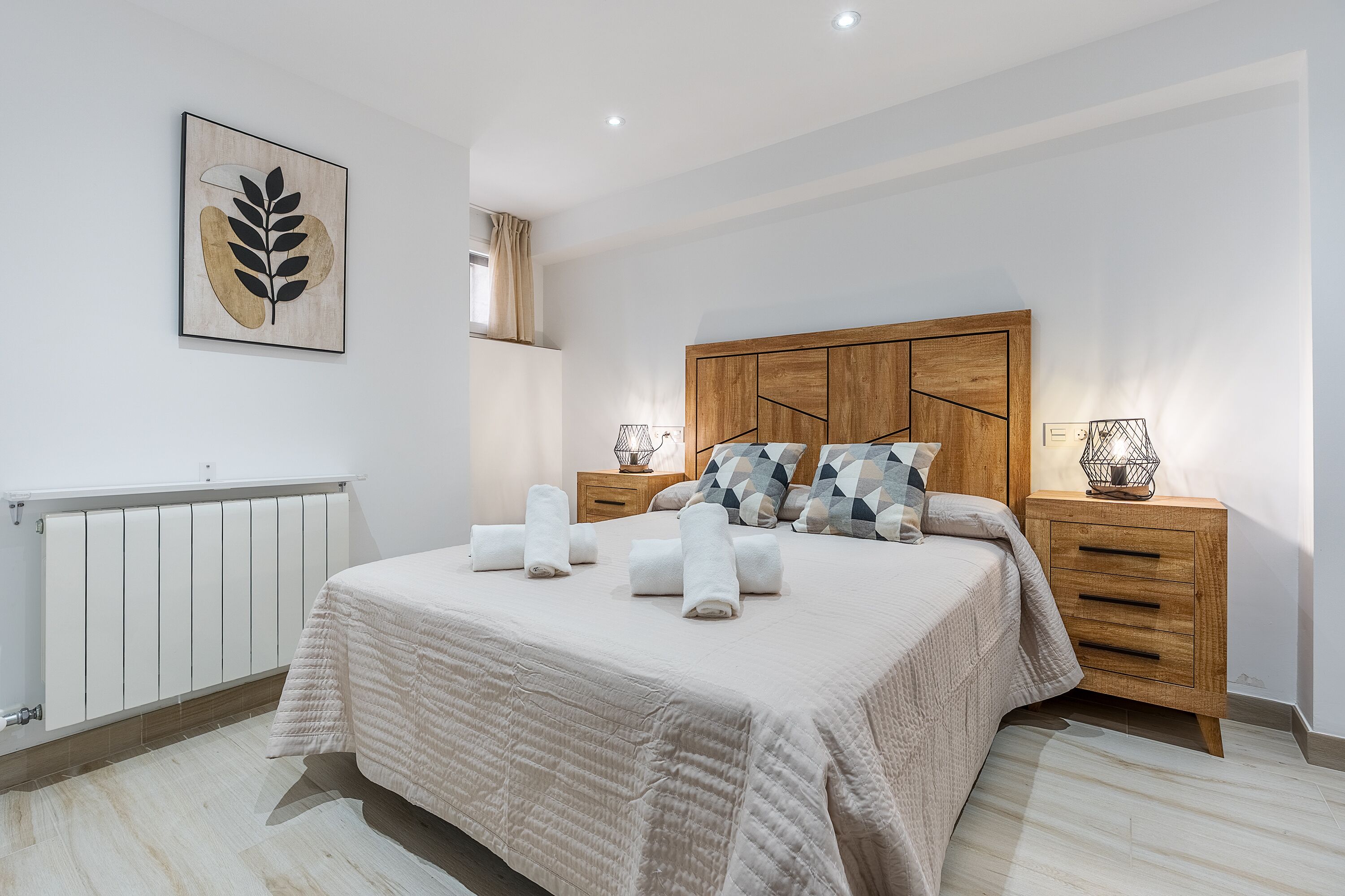 A bedroom with a bed, bedside tables, a radiator, and a wall-mounted artwork.