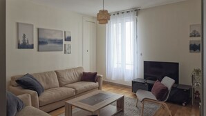 Una sala de estar con un sofá, sillones, una mesita de centro, un televisor y obras de arte en las paredes.