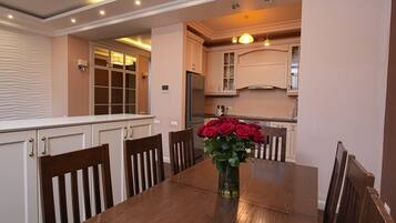 Un coin repas avec une table et des chaises en bois, un vase de roses rouges et, au fond, une cuisine.