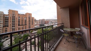 A balcony with a table and chairs, overlooking a cityscape with high-rise buildings.