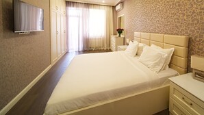 A hotel room with a large bed, a flat-screen TV mounted on the wall, a bedside table with a lamp, and a patterned wallpaper.