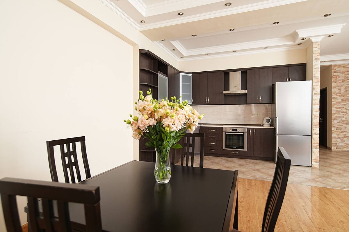 Una cocina moderna con armarios oscuros, un refrigerador de acero inoxidable y un florero sobre la mesa de comedor.