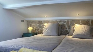 A bedroom with a stone headboard, two beds, a nightstand with a lamp, and a beach-themed towel. - Above the rooftops of Antibes (Antibes)