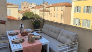 An outdoor balcony with a table set for dining, a cushioned seating area, and a view of surrounding buildings. - Above the rooftops of Antibes (Antibes)