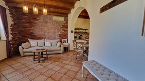A living room with a sofa, a round table, and a bench. There is a kitchen area visible through an archway. - Apartment  (Koper)