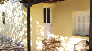 A narrow stone pathway leading to a yellow building with a white door and window shutters. - Nakou's House-Το σπίτι του Νάκου (Liopraso)