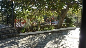 A paved courtyard with stone tiles, a tree, and a metal fence. - Nakou's House-Το σπίτι του Νάκου (Liopraso)