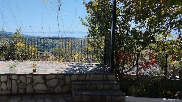A stone patio with potted plants, a metal railing, and a view of distant hills. - Nakou's House-Το σπίτι του Νάκου (Liopraso)