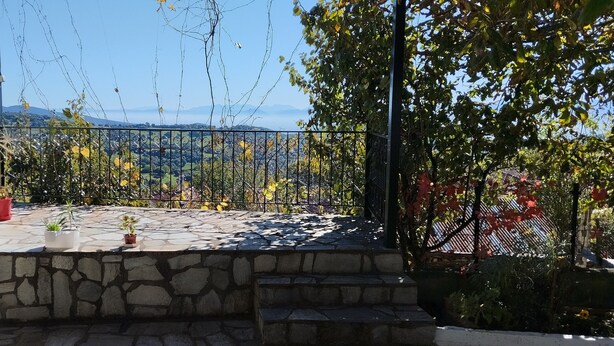 Une terrasse dallée de pierres, agrémentée de plantes en pot et dotée d’une rambarde en métal, qui offre une vue sur un paysage montagneux.
