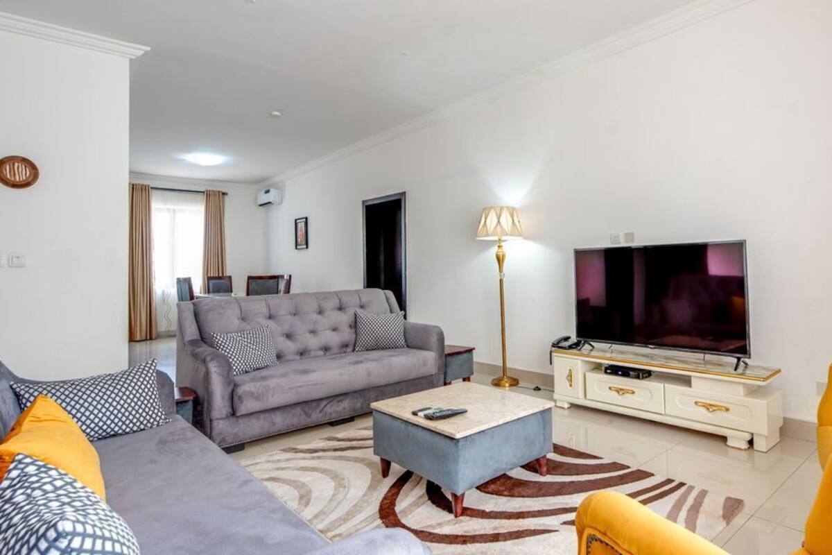 Una sala de estar con un sofá gris, un sillón amarillo, una mesa de centro, un televisor y una lámpara.