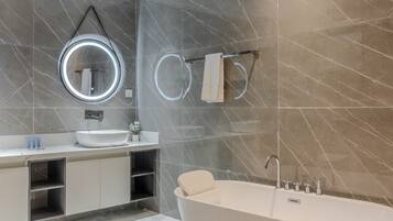 Un baño moderno con una bañera independiente, un espejo redondo con iluminación integrada y un perchero para toallas.