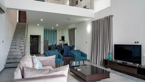 A modern living room with a sofa, coffee table, and TV. There is a staircase leading to an upper level. - Lakowe Lakes Hotel Golf and Country Estate by NEWMARK (Lekki)