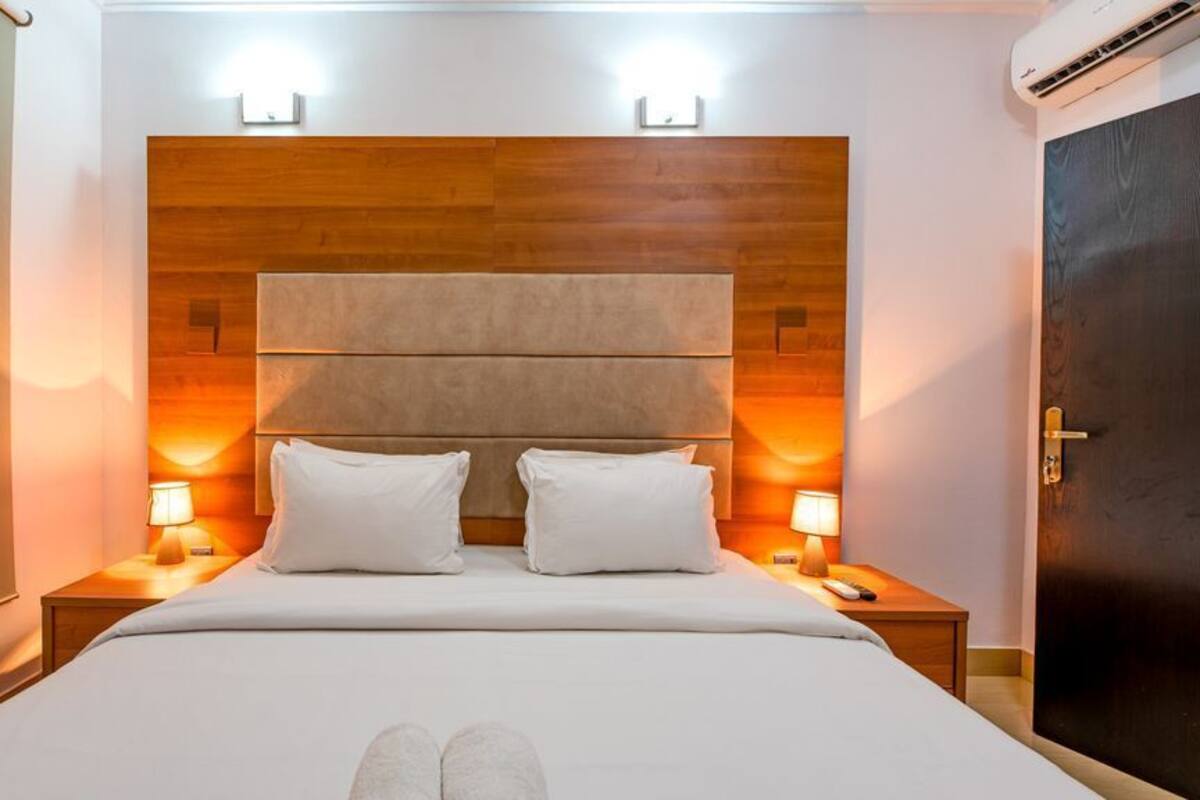 Habitación de hotel con una cama grande, dos lámparas de noche, un cabecero de madera y una puerta oscura.