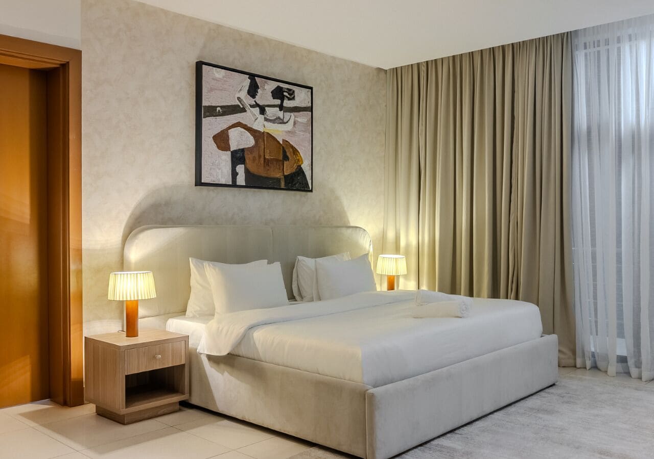 Ein Hotelzimmer mit einem großen Bett, zwei Nachttischen inklusive Lampen, einer Kopfteil und einem Gemälde an der Wand.