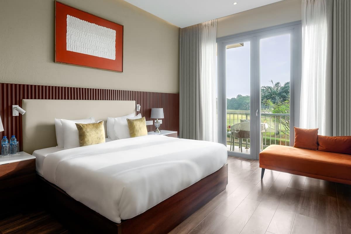 Habitación de hotel con una cama grande, un sofá, un balcón con vistas y una obra de arte enmarcada en la pared.