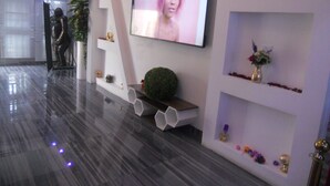 A modern lobby with a flat-screen TV mounted on the wall, a reception desk, and a decorative wall with shelves and plants. - Gold Crown international Hotel (Johannesburg South)
