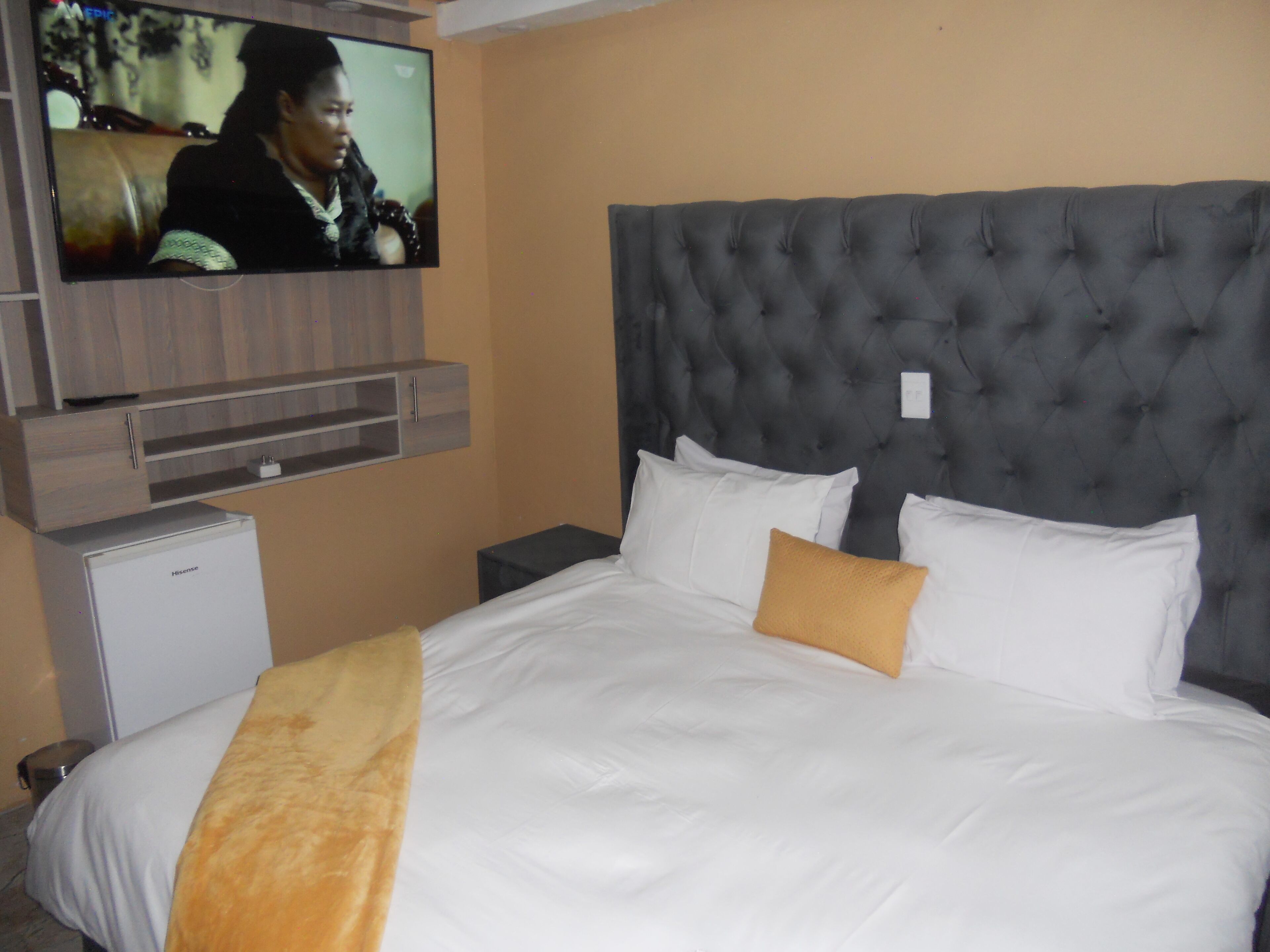 A hotel room with a large bed, a television mounted on the wall, and a small refrigerator.