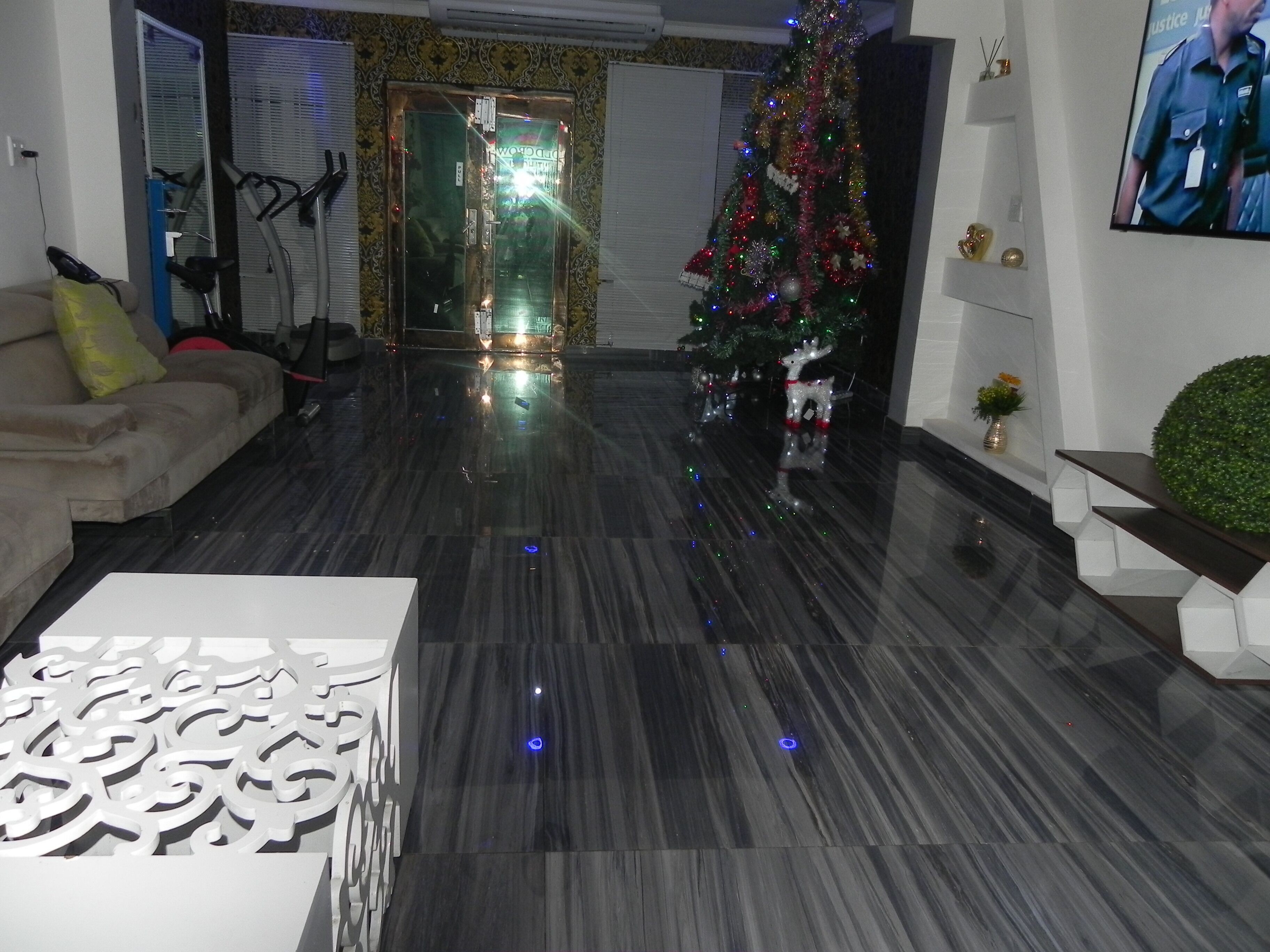 Un salon moderne avec un sol en marbre foncé, un panneau décoratif blanc, un canapé beige, un sapin de Noël et un téléviseur fixé au mur.