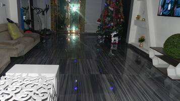 A modern living room with a dark marble floor, a white decorative panel, a beige sofa, a Christmas tree, and a television on the wall.