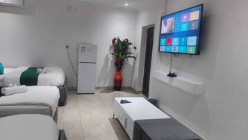 A hotel room with two beds, a small table, a TV mounted on the wall, a refrigerator, and a potted plant.