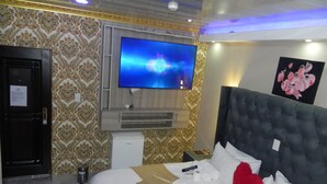 A hotel room with a large bed, a television mounted on the wall, a minibar, and a door with a sign. - Gold Crown international Hotel (Johannesburg South)