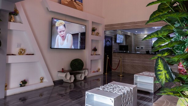 A modern hotel lobby with a flat-screen TV mounted on the wall, a reception desk, and a reception area with a counter and chairs. - Gold Crown international Hotel (Johannesburg South)