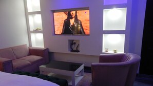A modern living room with a flat-screen TV mounted on the wall, a sofa, a chair, and a coffee table. - Gold Crown international Hotel (Johannesburg South)