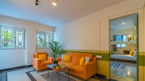 A modern living room with a sofa, armchair, and coffee table. There is a potted plant and a window with a view of greenery. - Zostel Bangalore (Koramangala) (Bengaluru)