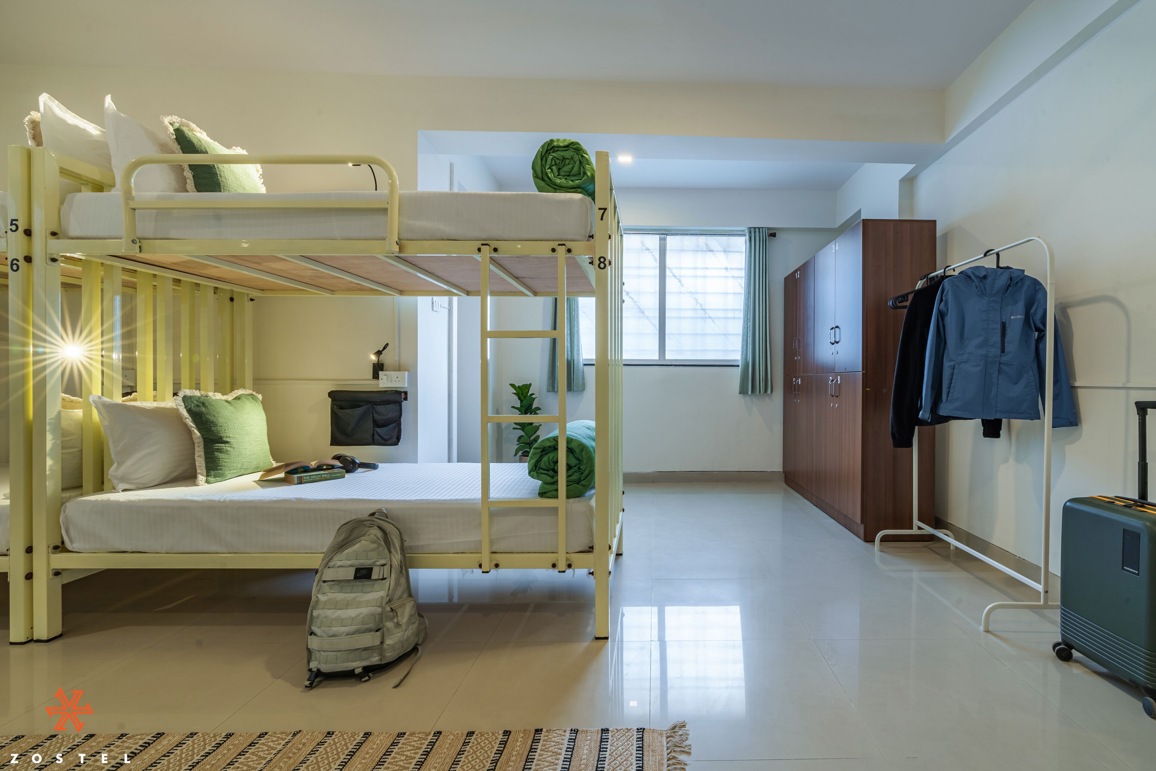 A bunk bed room with a suitcase and a backpack on the floor, a wardrobe, and a window with curtains.