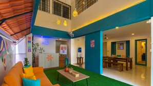 A modern interior with a green artificial grass floor, a wooden coffee table, and a bright orange sofa with blue cushions. - Zostel Bangalore (Koramangala) (Bengaluru)