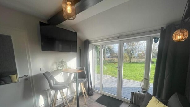 A modern living room with a sofa, a dining table with chairs, and a large sliding glass door leading to a garden. - Gryt Home Appartment L Nähe Nordsee (Ramhusen)
