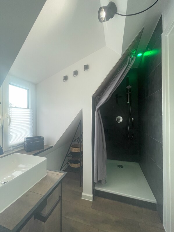 Un baño moderno con ducha, lavamanos y una escalera que conduce a un nivel superior.