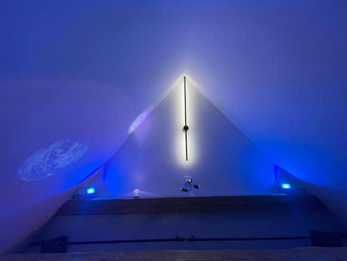 Ein Zimmer mit schrägem Dach, einer zentralen Leuchte und zwei seitlichen Lampen.