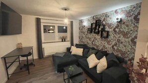 A modern living room with a dark sofa, a small table, and a patterned wall. - Gryt Home Fewo XXL Nähe Nordsee (Ramhusen)