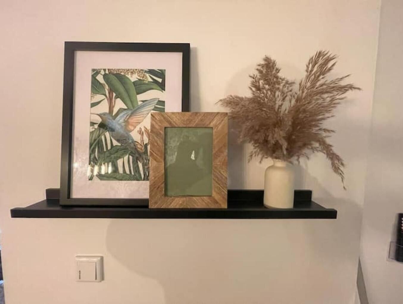 A shelf with a framed picture of a bird, a vase with dried plants, and a small framed item.