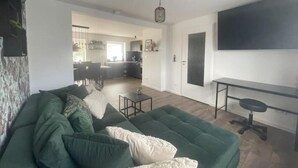 A modern living room with a green sofa, a dining area, and a kitchen in the background. - Gryt Home Fewo XXL Nähe Nordsee (Ramhusen)