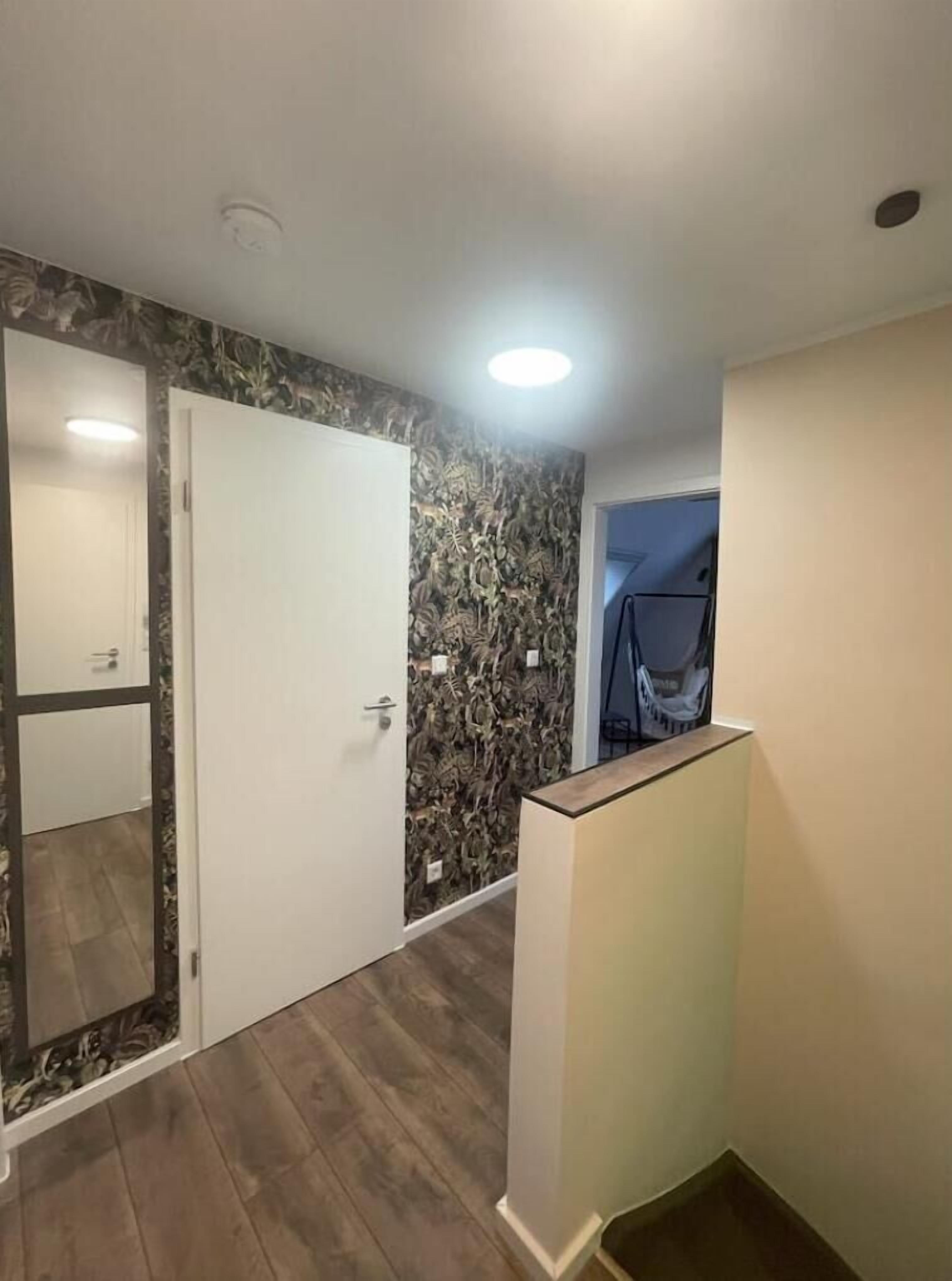Un couloir avec une porte blanche, un mur à motifs et une petite table.