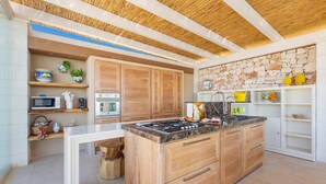A modern kitchen with wooden cabinets, a central island, and a stone wall backsplash. - 3666 Ca' Della Roccia by Perle di Puglia (Ostuni)