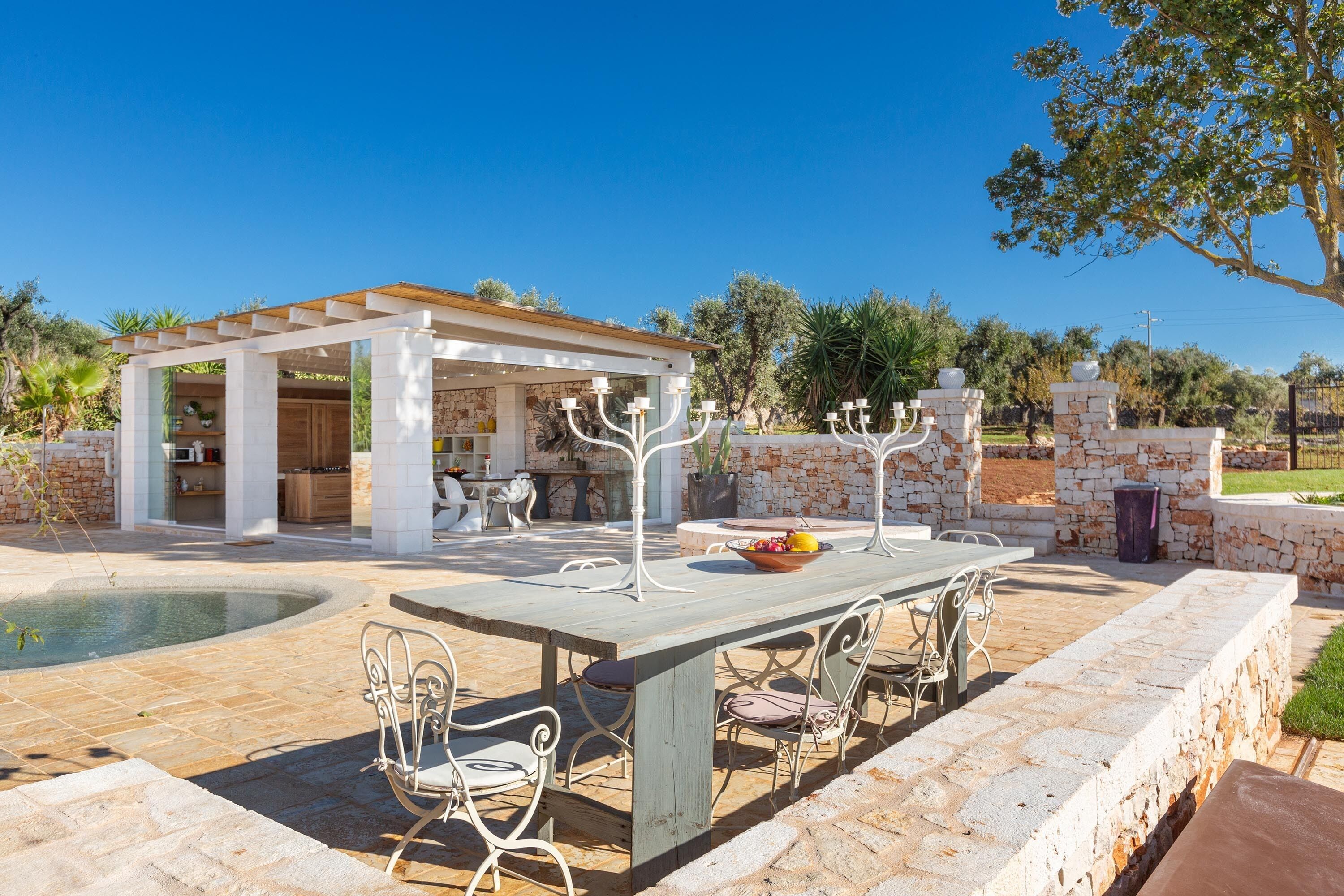 Ein Außenbereich mit Terrasse, Pool, Steinmauern und einer Pergola mit Essmöbeln.